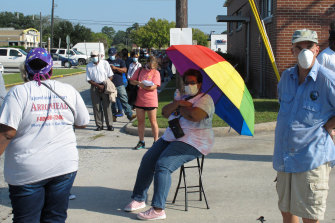 Crystal Clark sits on a folding stool while holding an umbrella for shade as she waits in line to vote early in Savannah, Georgia.