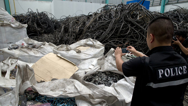 A Thai police officer photographs wrecked fitness bands during a raid at a factory accused of importing and processing electronic waste in the suburbs of Bangkok.