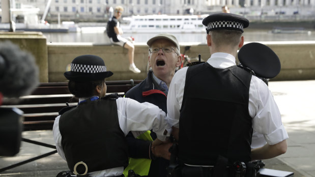 A Julian Assange supporter who was taking part in a coronavirus anti-lockdown, anti-vaccine, anti-5G and pro-freedom protest is held by police officers before being taken away, near Scotland Yard.