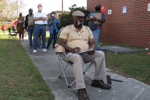 Richard Williams sits in a folding chair, filling out paperwork, as he waits in line to vote early in Savannah. Black people are going to the polls by the thousands and waiting in lines for hours to vote early.