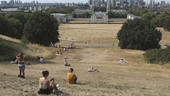 People sit on the sun-parched grass in Greenwich Park