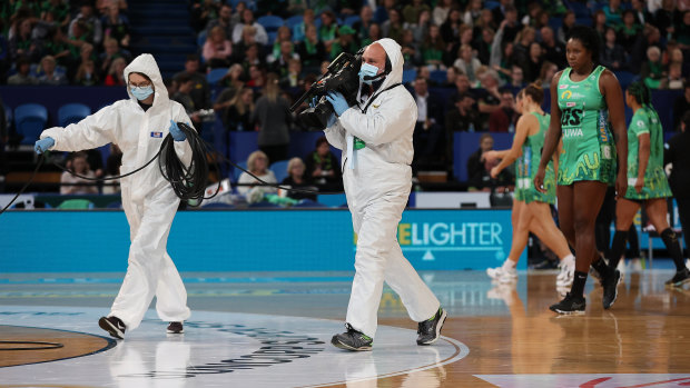 Two members of the media walk across the court wearing PPE during the round five match between the Fever and the Giants. 