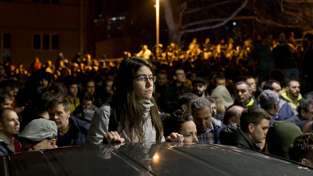 A protester stands as a crowd gathers at an entrance to the state-run TV headquarters in Belgrade, Serbia, on Saturday.