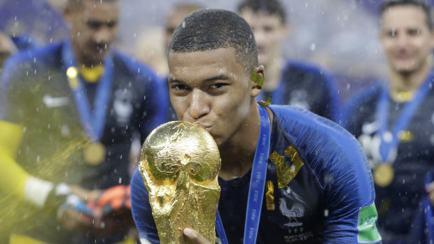 French player Kylian Mbappe kisses the World Cup trophy.
