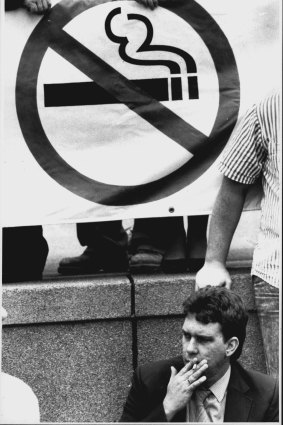 A man smokes in front of an Anti-Smoking sign.