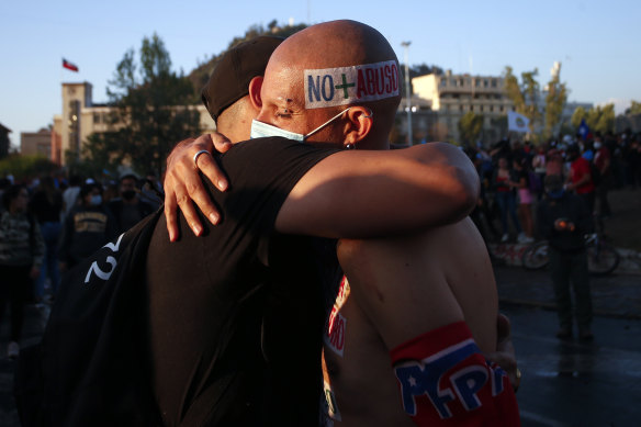 Two men, one with a head sticker reading "No more abuse", embrace each other in Santiago on the day Chileans voted to create a new constitution.