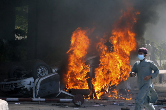 A man runs past a burning car set on fire by angry supporters of Pakistan’s former prime minister Imran Khan during a protest against his arrest, in Peshawar.