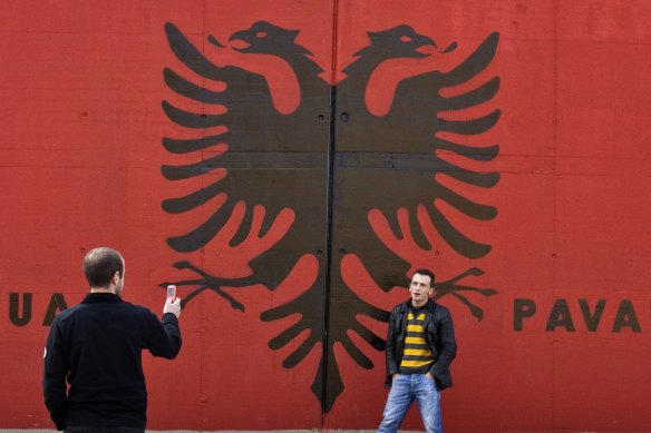 Ethnic Albanian man poses for a picture in front of a giant Albanian flag.