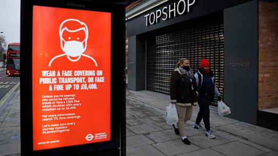 People walk past a closed brach of Topshop next to a bus stop coronavirus information sign on Oxford Street in London.