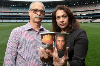Jayant and Reva Chitnis at the MCG, holding coffee cups with an image of their missing son, Tej and his car. 