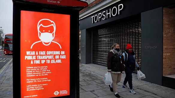 People walk past a closed brach of Topshop next to a bus stop coronavirus information sign on Oxford Street in London.