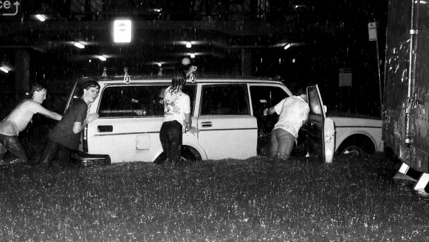 Motorists and passers-by struggle to move a car to higher ground in the stricken Haymarket area.
