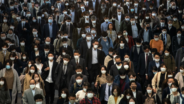 Commuters, mostly wearing face masks, walk through Shinagawa train station, Tokyo, on Wednesday.