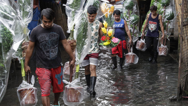 Workers carry plastic plants over flooded waters as heavy monsoon rains continue in Manila, Philippines.