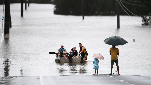 A father and his young daughter watch as people move through floodwater in Logan, south of Brisbane.  