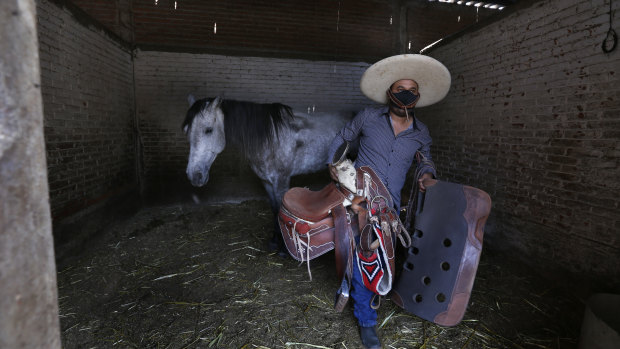 Wearing a mask, Leonardo Flores, takes the saddle off a horse called Rabbit in the stables of the Iztapalapa Charro riding arena in Mexico City.