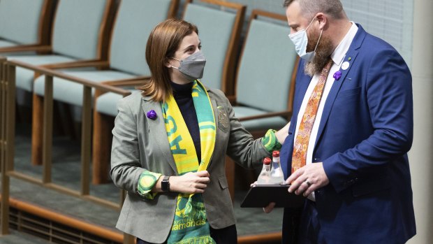 Minister for Aged Care and Minister for Sport Anika Wells wears a green and gold scarf and a purple flower on her jacket, while Labor MP Dan Repacholi wears a purple flower in his jacket pocket. 