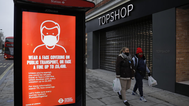 People walk past a closed brach of Topshop next to a bus stop coronavirus information sign on Oxford Street in London.