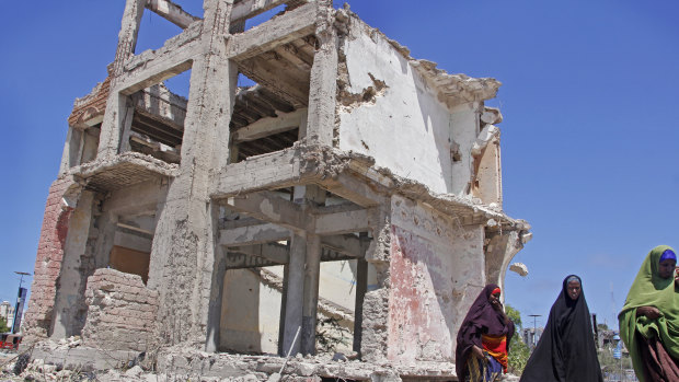 Somali women walk past a destroyed building after a suicide car bomb attack in the capital Mogadishu, Somalia.