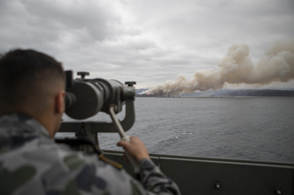 Seaman Boatswains Mate Malik El-Leissy watches a burning fire from HMAS Adelaide as the ship arrives at Eden to assist with bushfires in 2020.
