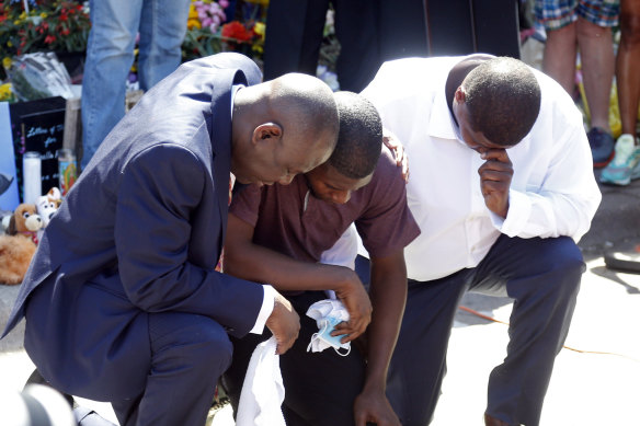 Quincy Mason, centre, the son of George Floyd, and family lawyer Ben Crump, left, kneel, as they visited the memorial on the site where Floyd was arrested and then died in police custody. 