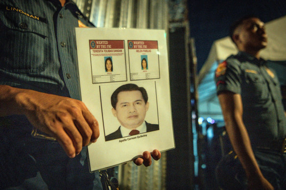 Police holding a poster with pictures of the fugitive Apollo Quiboloy and his associates outside the gates of the Kingdom of Jesus Christ compound.