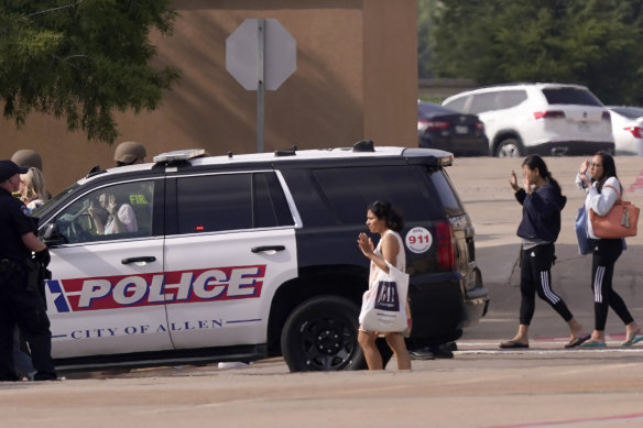 People raise their hands as they leave a shopping centre after the shooting in Allen, Texas.