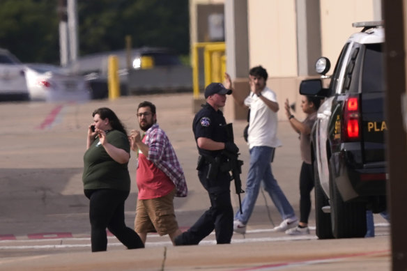 People raise their hands as they leave a shopping centre in Allen, Texas, following the shooting.