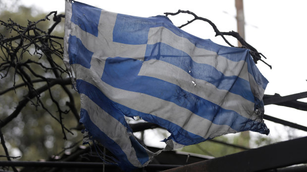 A tattered and charred Greek national flag hangs from a burned-out house in Mati east of Athens.