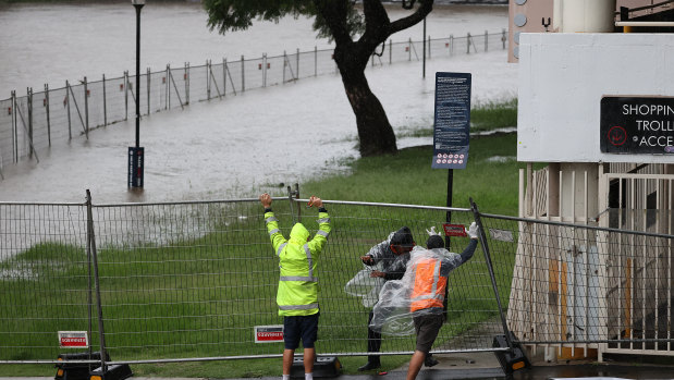 Men struggle to lift a fallen fence that surrounds the Powerhouse Museum site as the Parramatta River overflows.