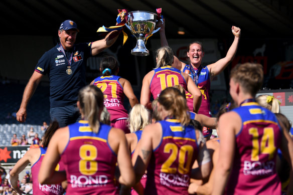 Brisbane coach Craig Starcevich lifts the AFLW premiership cup with skipper Breanna Koenen, much to the delight of the Lions players.