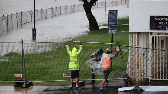 Men struggle to lift a fallen fence that surrounds the Powerhouse Museum site as the Parramatta River overflows.