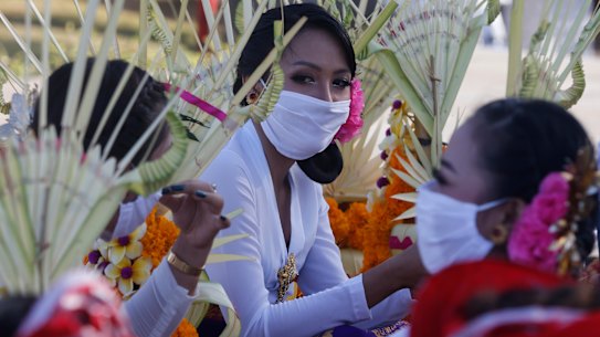 Women wearing face masks wait to join a parade in Bali, Indonesia.