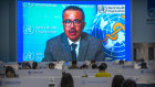 Journalists work as video of World Health Organisation chief Tedros Adhanom Ghebreysus is played on a giant screen.