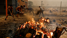 Young people try to extinguish a fire outside a house as wildfires surround a Spanish village.