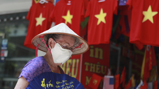 A woman walks past a row of T-shirts printed with Vietnamese flags in Hanoi. For 99 days, Vietnam seemed to have defeated the coronavirus, but now a new outbreak in the city of Da Nang has grown to dozens of cases in six cities.