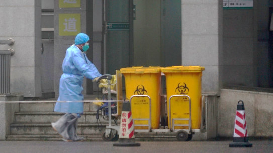A staff member moves bio-waste containers past the entrance of the Wuhan Medical Treatment Center in Wuhan, China, where some people infected with a new virus are being treated.