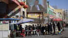 Residents line up at a security checkpoint at the Hotan Bazaar  in western China’s Xinjiang region where a screen shows Chinese President Xi Jinping.