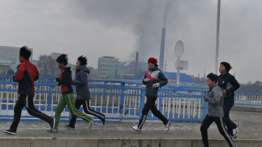 Young joggers pass by as smokes billows from the stack of the Pyongyang Power Plant in Pyongyang, North Korea. 