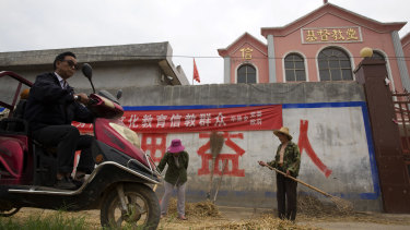 A man rides past workers tossing hay outside a church with part of a slogan that reads "Educate the believers with excellent Chinese traditional culture" near the city of Pingdingshan in central China's Henan province. 