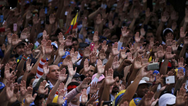 Anti-government protesters hold their hands up during the symbolic swearing-in of Juan Guaido in Caracas on Wednesday.