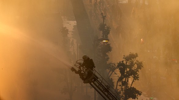 A firefighter sprays a fire at a small shopping centre amid anti-government protests in Santiago on Monday.