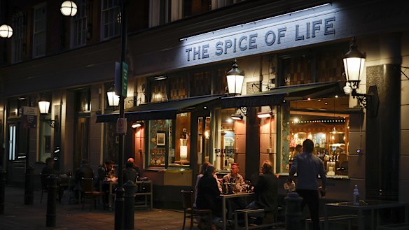 Customers sit in an outside area of a bar in Soho in London.