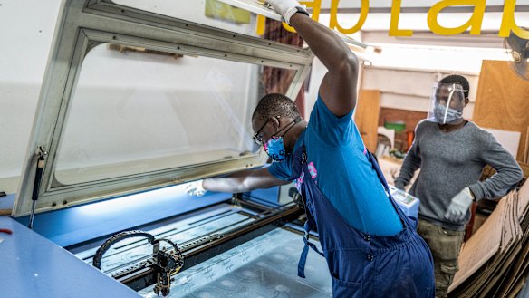 Mohamed Gueye, centre, and Idrissa Sall, right, use a laser cutter to make protective face shields.