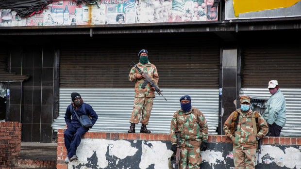 Soldiers stand guard as residents of Alexandra Township begin cleaning up after several days of looting.