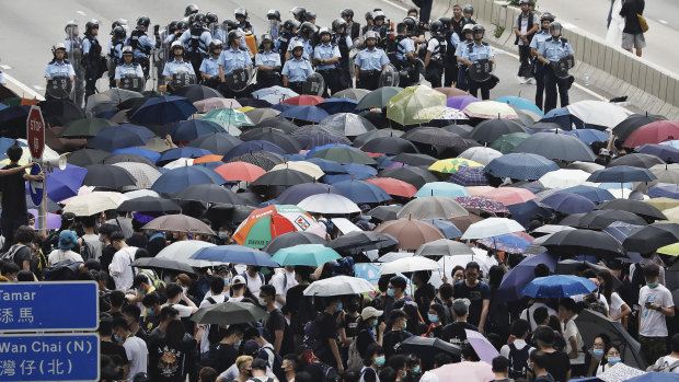 Policemen in riot gear stand behind protesters using umbrellas to shield themselves as they gather outside the Legislative Council in Hong Kong.