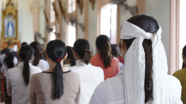 A woman wearing a white head band, traditionally worn by relatives of a deceased person during the funeral in Vietnam to show sign of mourning, attends a Sunday Mass at Phu Tang church in Yen Thanh district, Nghe An province, Vietnam. 