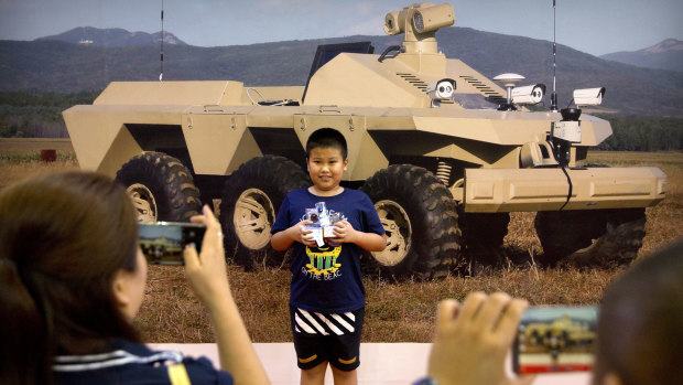 A boy poses for smartphone photos in front of a mural of a mobile tactical robot.