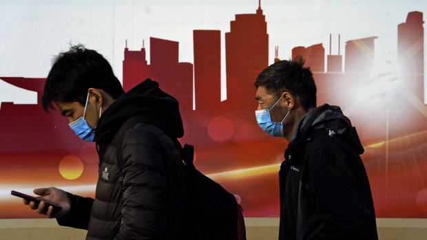 People wearing face masks to help curb the spread of the coronavirus walk by a mural depicting China's skyscrapers along a street in Beijing.