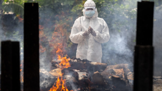 A relative in protective suit performs  rituals near the body of a loved one. during cremation in Gauhati, India.